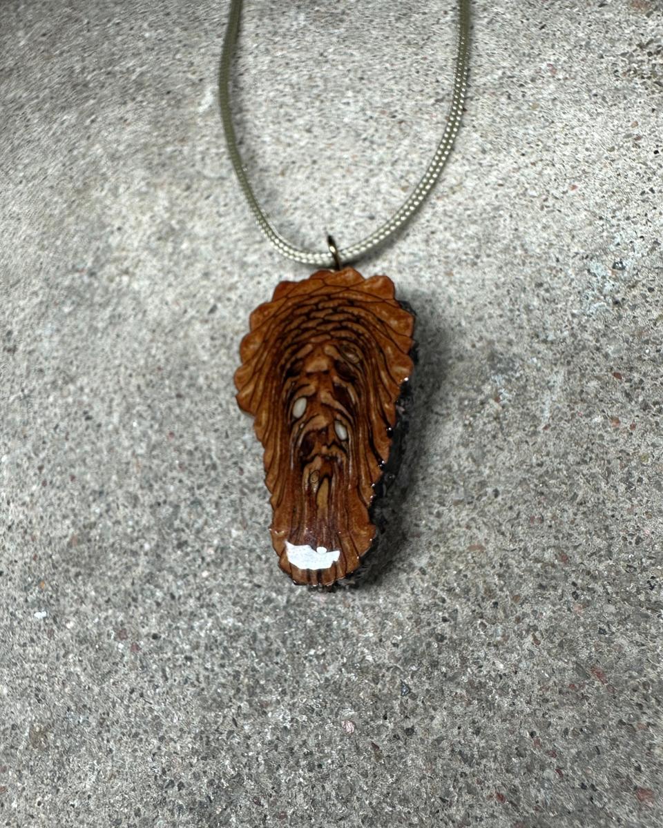 The other face of the pendant on its pale cord, honey-brown scales in stacked ridges with dark lines between them and two small white seed ends in the middle