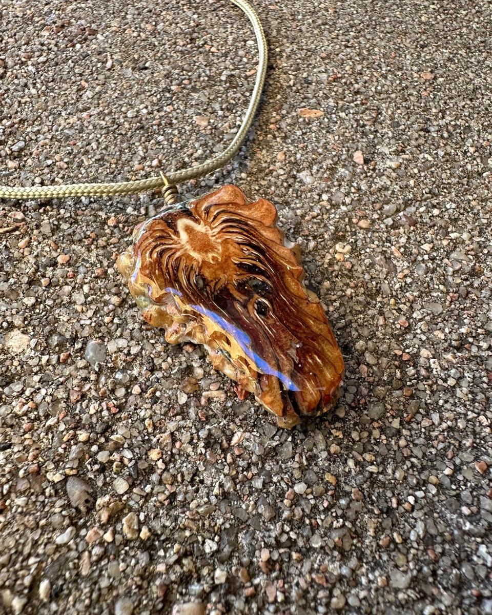The pendant lying at an angle on concrete with the cord looping away, showing the rounded resin edge with a violet flash along it and the rays sweeping across the face