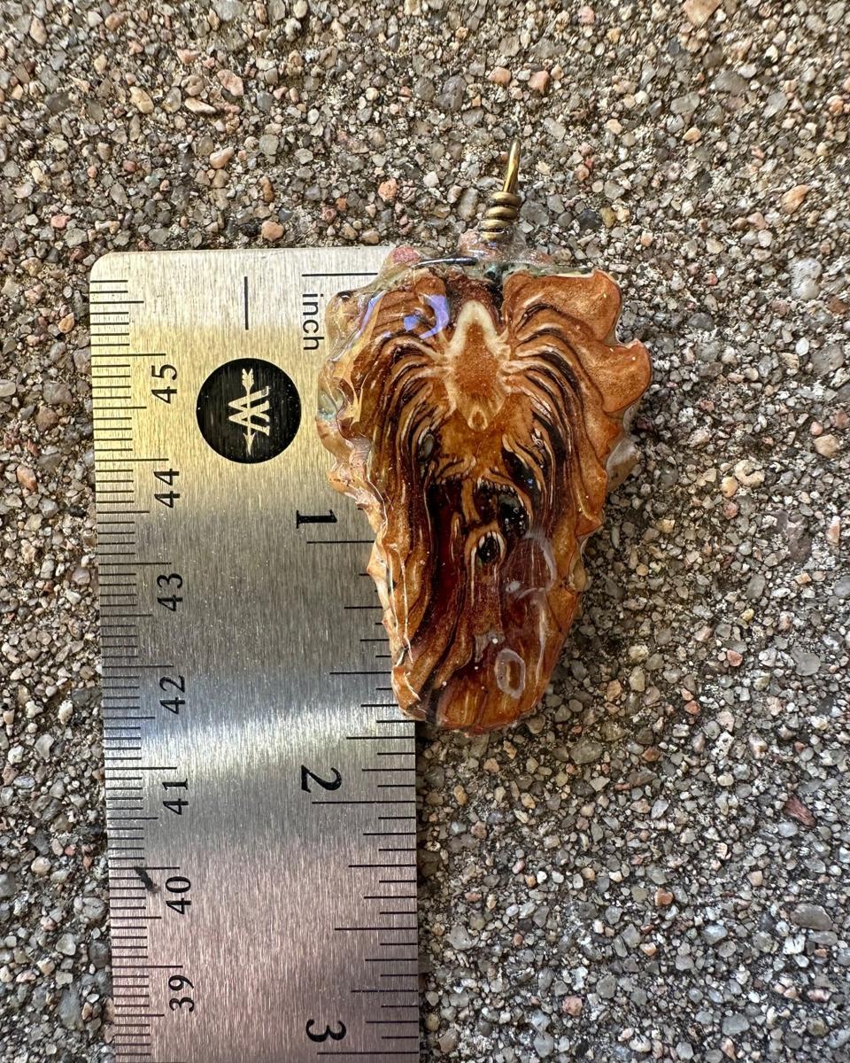 The pendant beside a steel ruler on concrete, showing the spade outline a little over two inches long