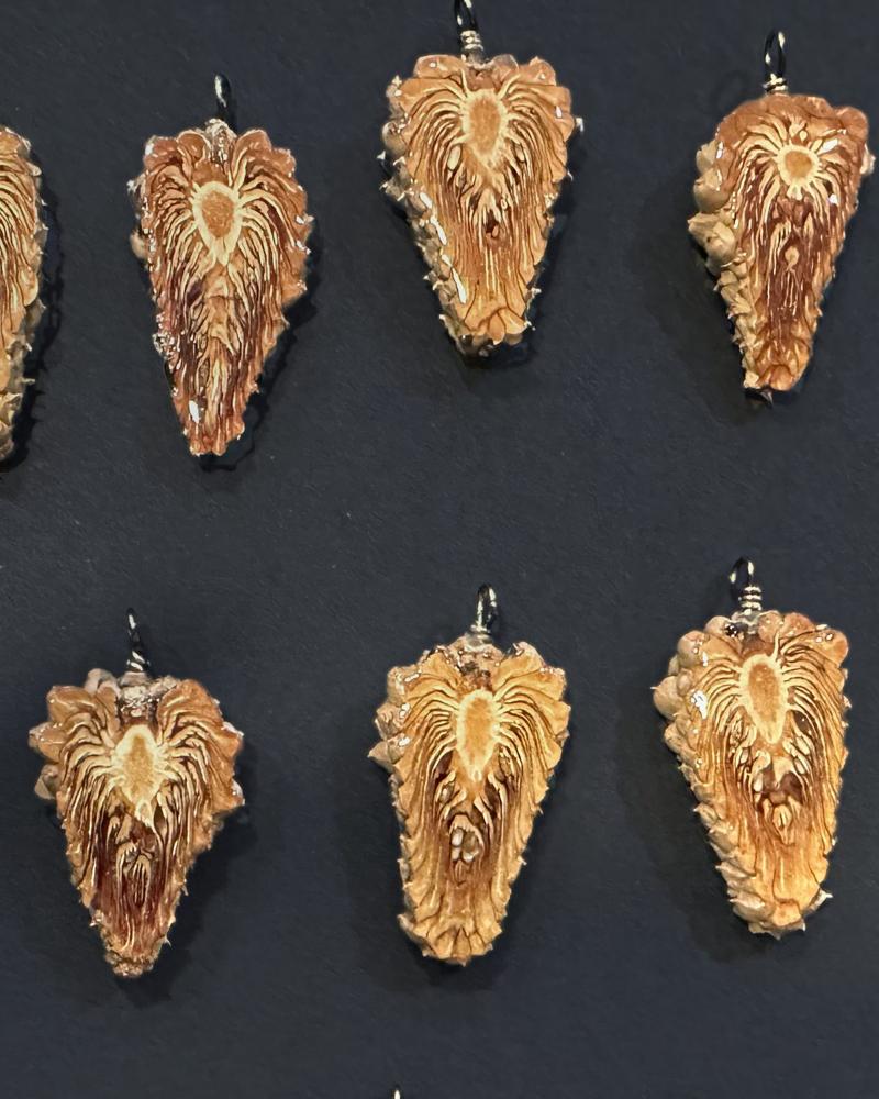 Rows of pine cone pendants laid out on dark slate paper: teardrop slices with sunburst cores, round cross-cuts, each with a small wire loop