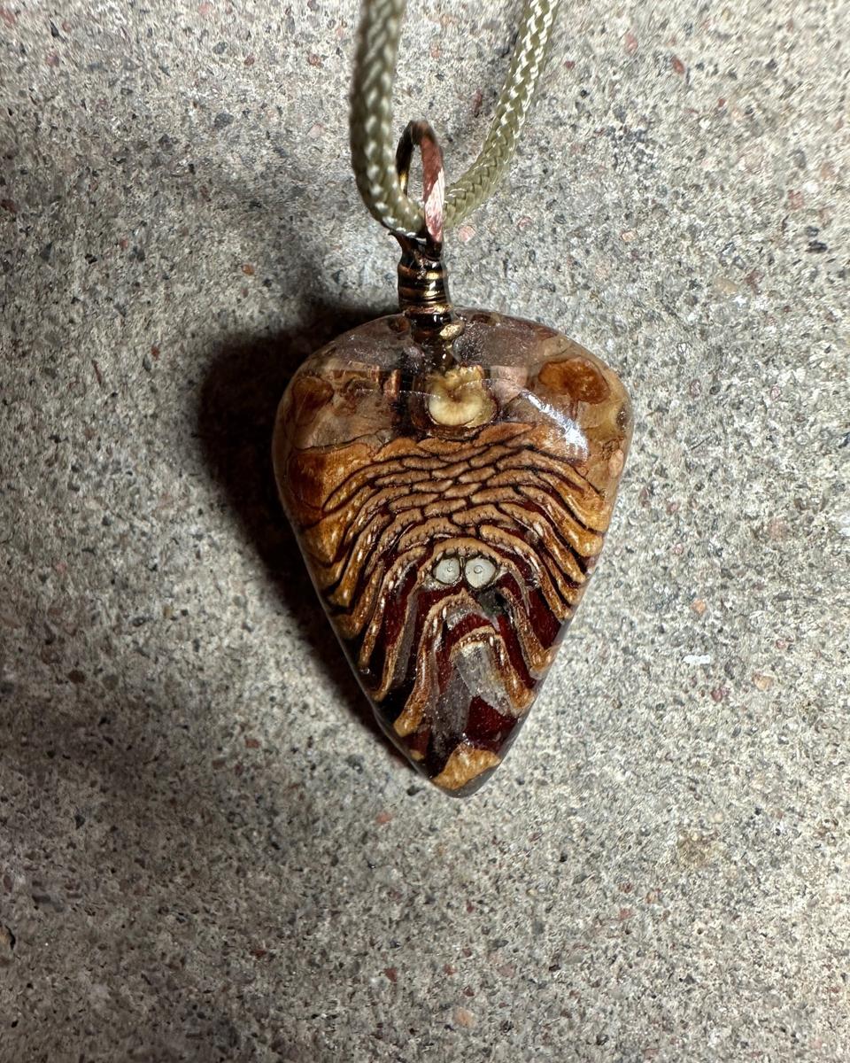 The other face of the pendant, paler tan and rust scales fanning out from the top with two small white rounds near the middle, under domed resin