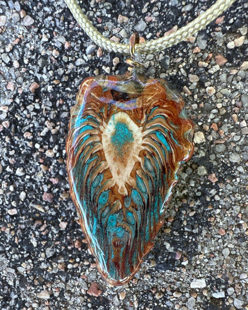 Teardrop pendant on a pale braided cord, with a cream feathered burst at the center and turquoise pooling between the scale rows under glossy resin