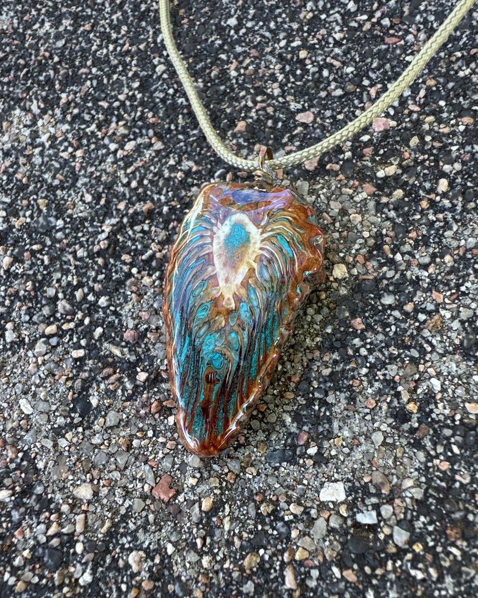 The other face of the pendant on its cord, showing a cream burst near the top over turquoise and brown